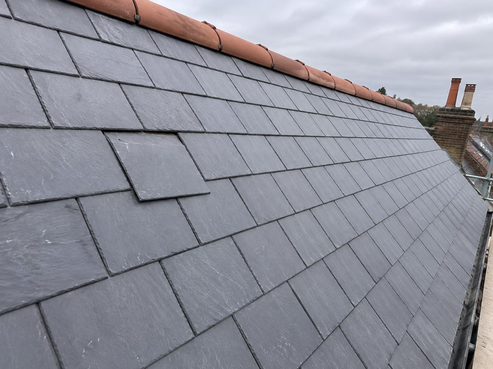Welsh slate roof in good condition with one slate slipped out of its row below a clay ridge